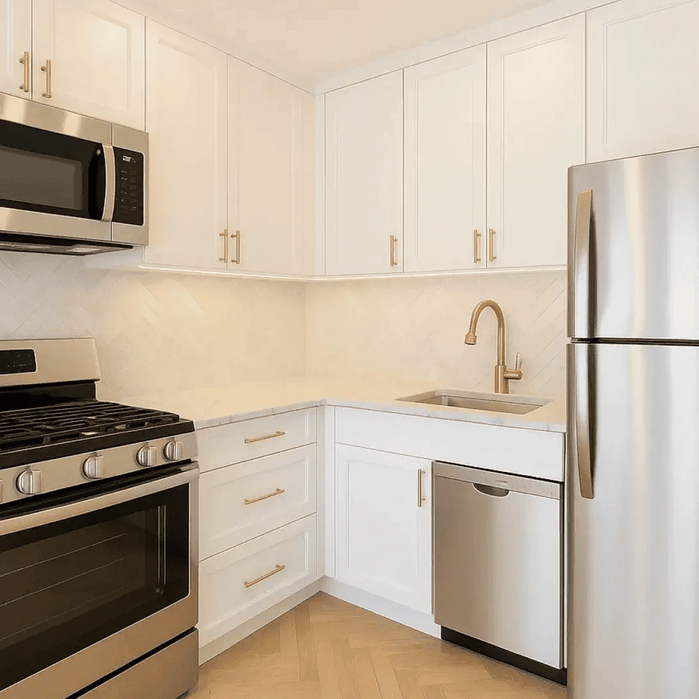 Bright kitchen with white shaker cabinets, herringbone backsplash, brushed-gold hardware, and stainless-steel appliances, part of a kitchen renovation on Hudson St, Hoboken NJ